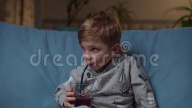 晚上，坐在舒适的沙发上喝果汁的学龄前儿童关门。 小孩喝蓝莓汁而不是